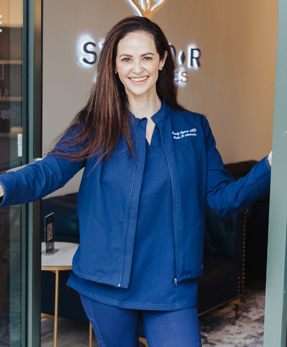 Smiling woman in scrubs at clinic entrance.