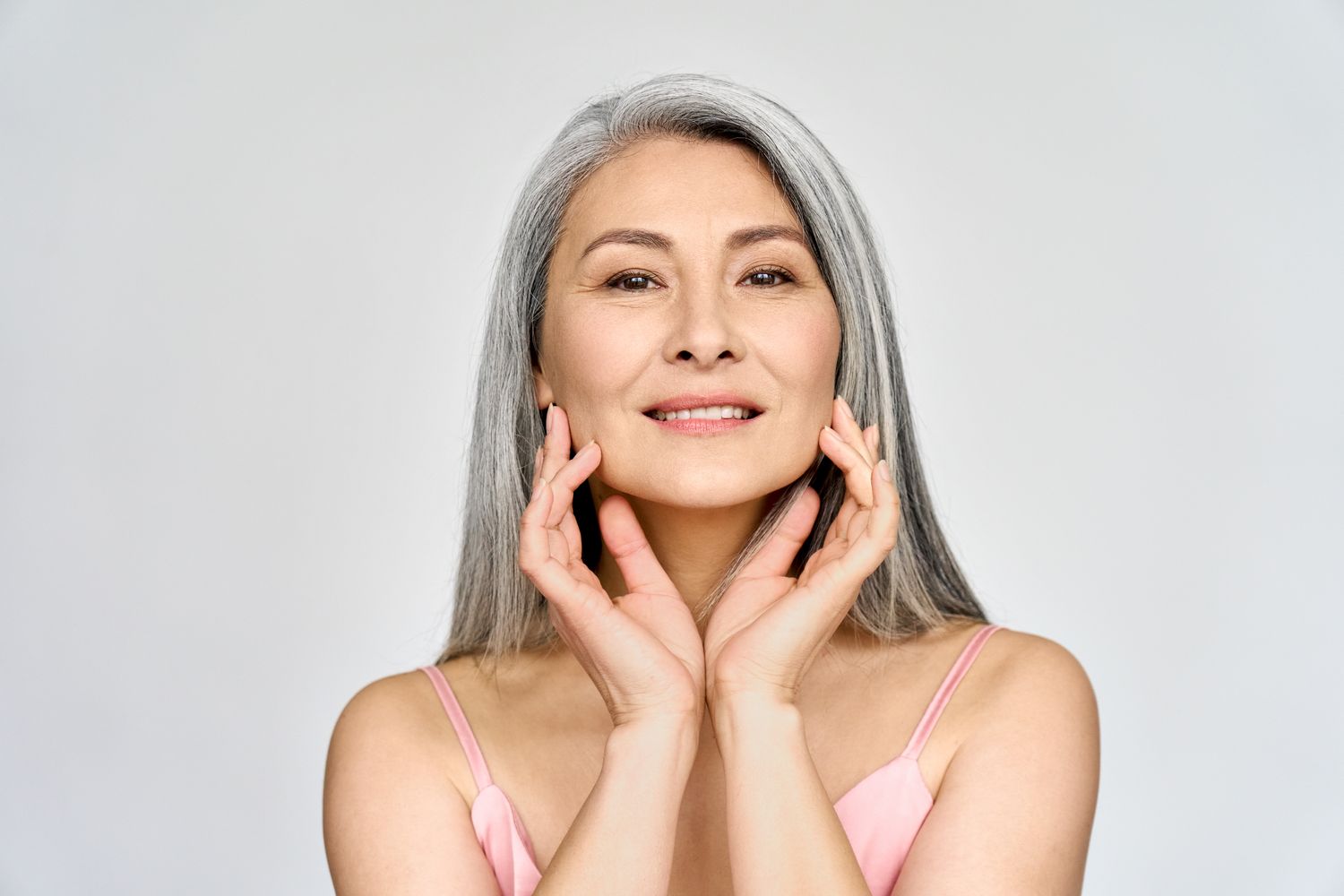 Portrait of gorgeous beautiful middle aged mature asian woman, senior older 50 year lady looking at camera touching her face isolated on white.